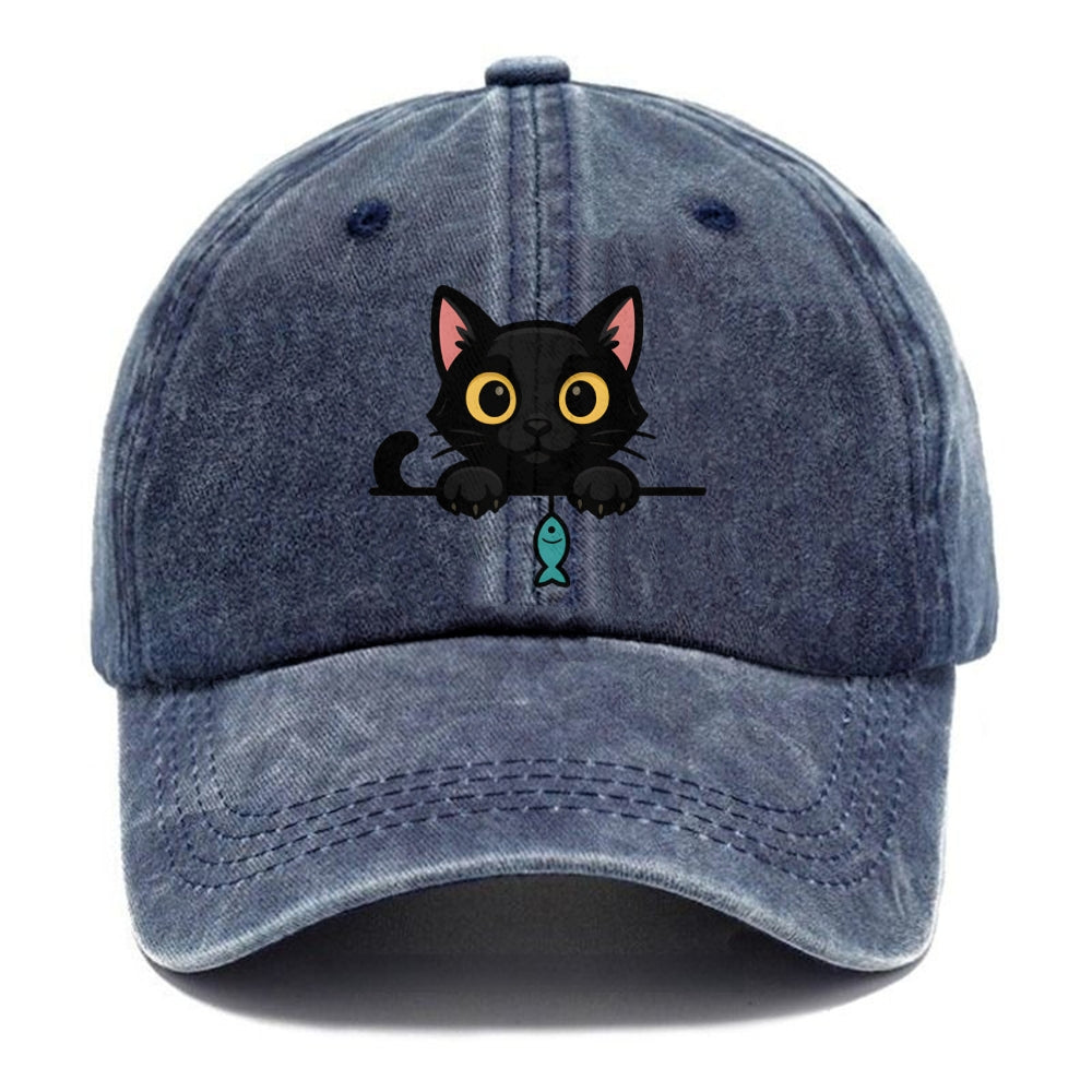 Midnight the black cat holding a tiny yarn ball between both paws while peeking Washed Cap