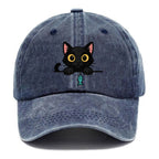 Midnight the black cat holding a tiny yarn ball between both paws while peeking Washed Cap