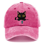Midnight the black cat holding a tiny yarn ball between both paws while peeking Washed Cap