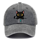 Midnight the black cat holding a tiny yarn ball between both paws while peeking Washed Cap